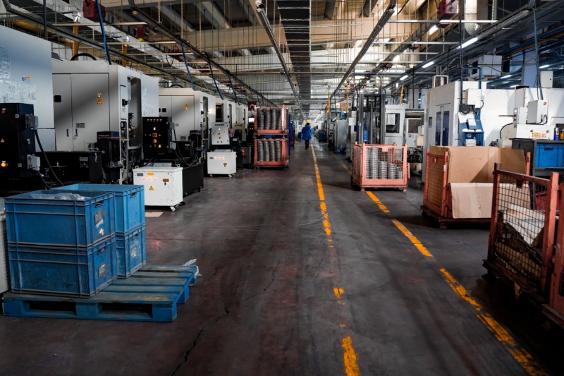 Blick durch eine industrielle Fertigungshalle mit einer Reihe von CNC-Maschinen und Materialtransportbehältern entlang des Gangs